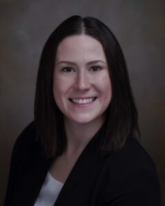 Smiling person with dark hair and suit.